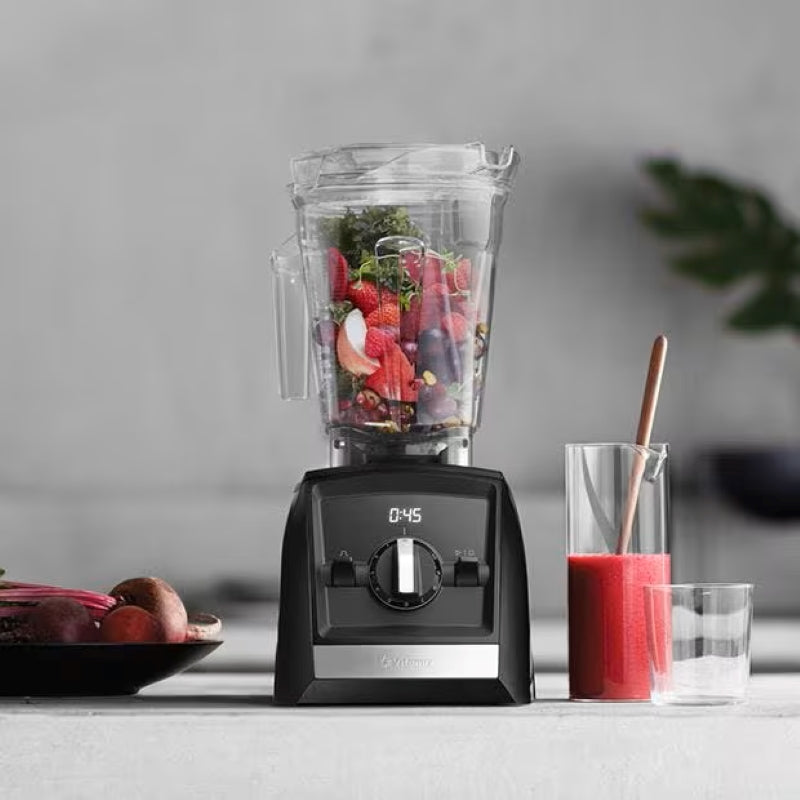Vitamix Ascent Series A2300i in the kitchen with fruits inside of it and a pitcher of smoothie on its side