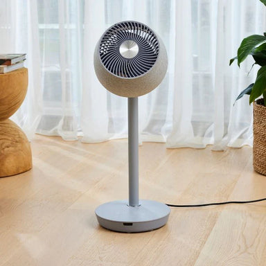 Stand fan on a wooden floor with light curtains in the background