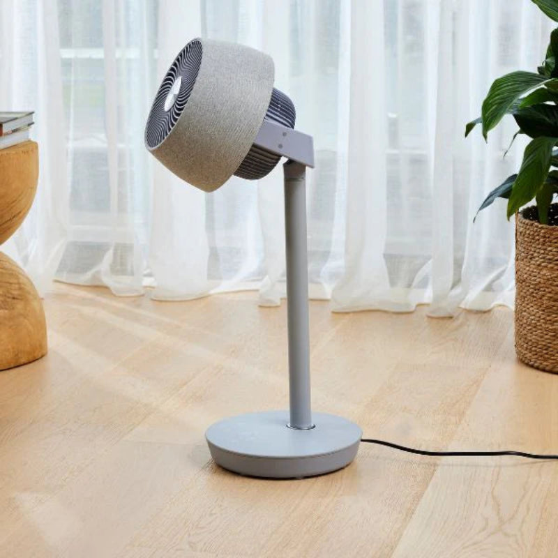 Gray floor fan on a wooden floor with white curtains in the background