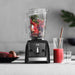 Vitamix Ascent Series A2500i in the kitchen with fruits and vegetables inside and a pitcher of smoothie on the side