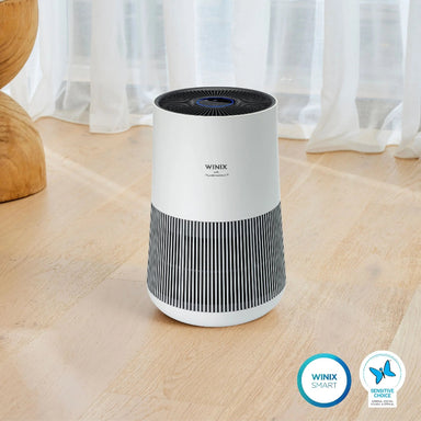 Winix air purifier on a wooden floor with curtains in the background